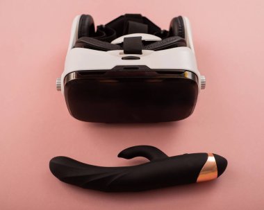 Black dildo and virtual reality helmet on a pink background. Masturbation concept with modern technology