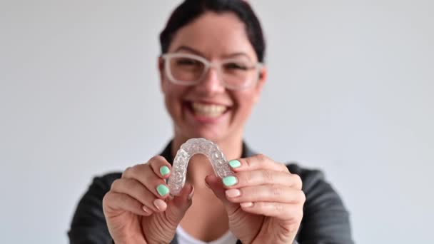 La mujer sonríe y sostiene un dispositivo de ortodoncia de plástico transparente para la corrección de mordeduras — Vídeos de Stock