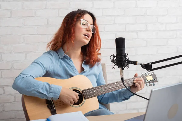 Eine Frau singt in ein Mikrofon und spielt die Gitarre live auf einem Laptop. Musikerin nimmt Videoblog auf — Stockfoto