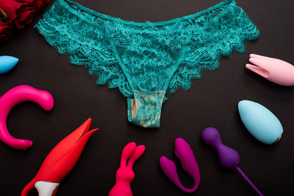 Top view of womens lace green panties red roses and different sex toys. Collection of multi-colored vibrators and underwear