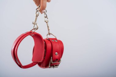 Beyaz arka planda kırmızı deri kelepçeler ve kadın elleri. BDSM aksesuarları
