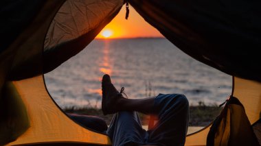 Gün batımında sahilde bir turist çadırında kadın bacakları. Kadın nehir kenarında yürüyüş yapıyor ve kamp yapıyor..