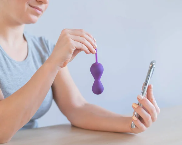 A female blogger recommends a kegel trainer online over the phone. A woman is holding a sex toy to strengthen the pelvic floor muscles — Stock Photo, Image