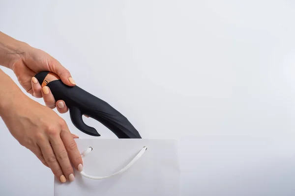 A woman makes a purchase and puts a dildo in a bag on a white background. Close-up of female hands with a black vibrator — Stok fotoğraf