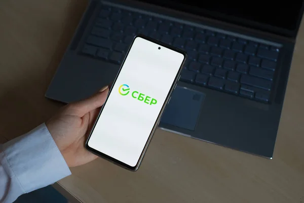 18 oktober 2020 Ryssland, Novosibirsk: En kvinna har en smartphone med den nya Sberbank-logotypen på skärmen — Stockfoto