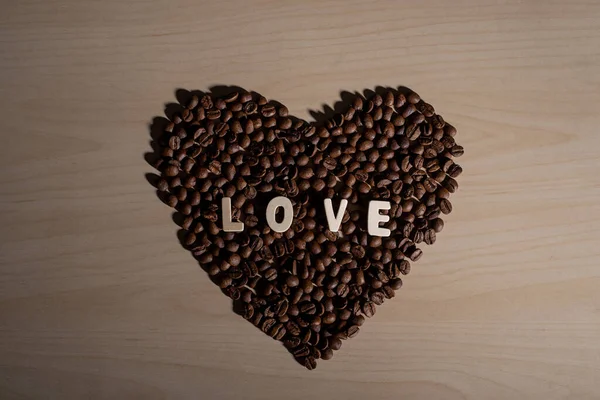 Kávová zrna ve tvaru srdce a nápis láska na dřevěném stole — Stock fotografie