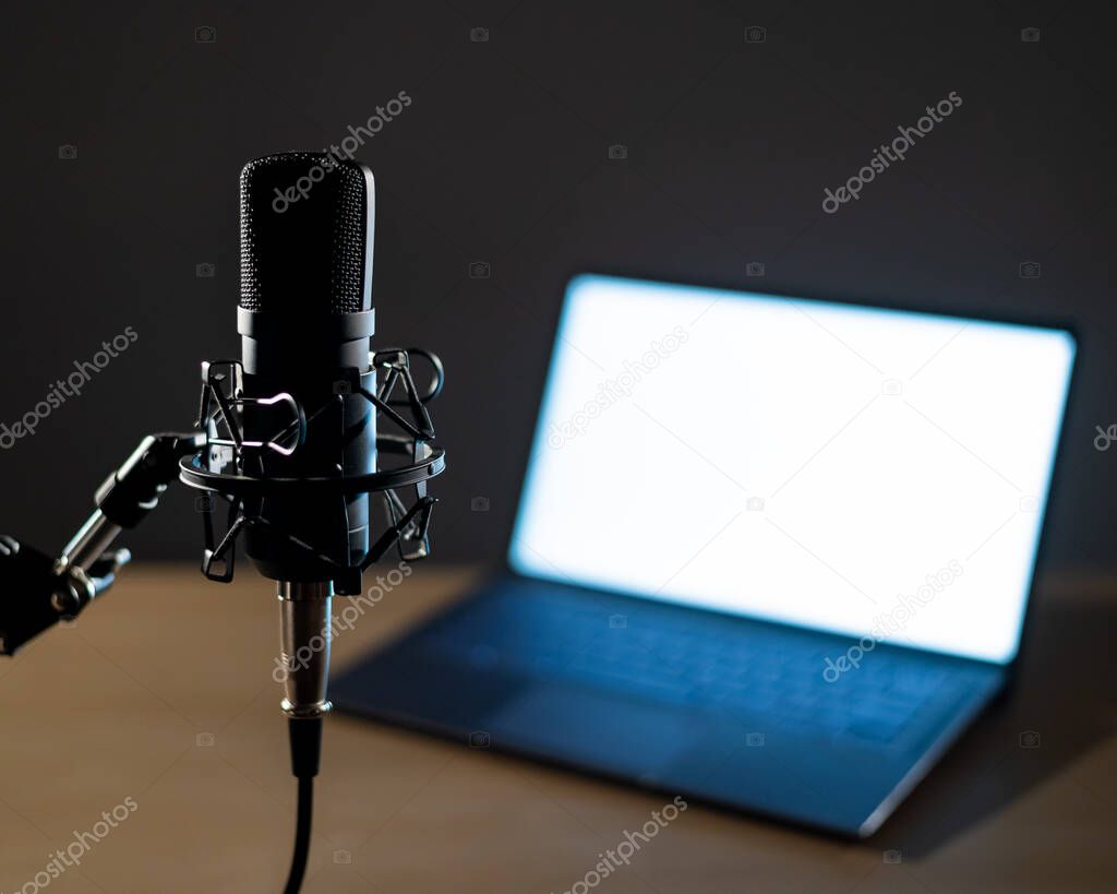 Professional microphone and laptop with white screen in the dark. Equipment in a recording and broadcasting studio