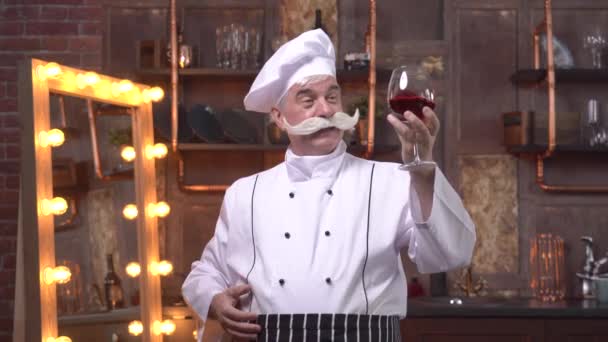 Пожилой шеф-повар дегустации красного вина на кухне — стоковое видео