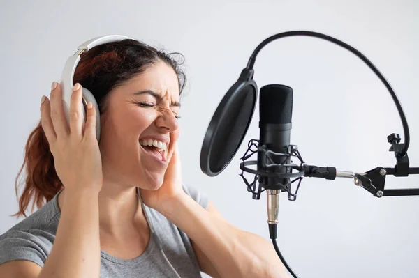 Una mujer con auriculares está grabando una canción en un estudio de grabación. Emocional chica canta con placer —  Fotos de Stock
