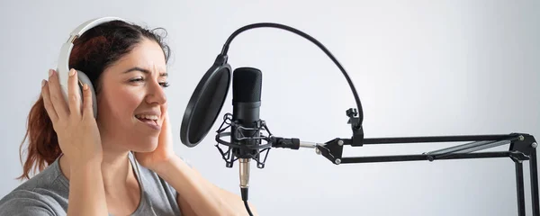 Una mujer con auriculares está grabando una canción en un estudio de grabación. Emocional chica canta con placer —  Fotos de Stock