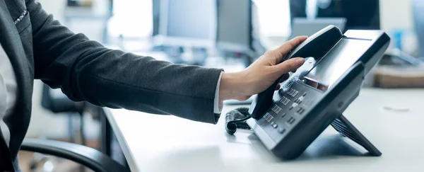 Primer plano de una empleada femenina mano en un teléfono fijo. Mujer coge un teléfono pulsador en el lugar de trabajo en la oficina — Foto de Stock