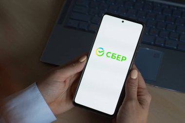 18 Ekim 2020 Rusya, Novosibirsk: Ekranda yeni Sberbank logosu olan bir kadın akıllı telefon tutuyor