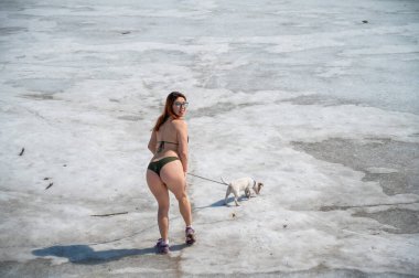 Bikinili bir kadın karda bir köpekle yürür.