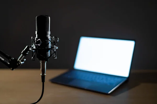 Professional microphone and laptop with white screen in the dark. Equipment in a recording and broadcasting studio — Stock Photo, Image