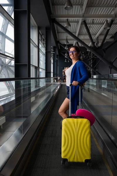 Kaukasierin auf einer waagerechten Rolltreppe mit einem Koffer am Flughafen. Ein Mädchen mit rosa Gepäck fährt auf einem fahrenden Bürgersteig — Stockfoto