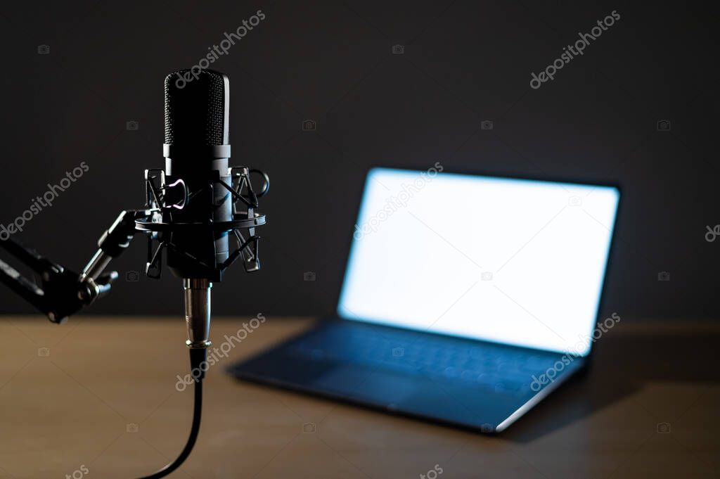 Professional microphone and laptop with white screen in the dark. Equipment in a recording and broadcasting studio