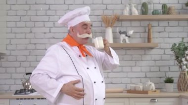 Neşeli sütçü bir bardak süt içer. Yaşlı bıyıklı bir adam mutfakta inek sütü içer.