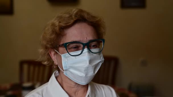 医師は赤外線温度計でマスクをしている高齢女性の温度を測定します。家から医務室へ — ストック動画
