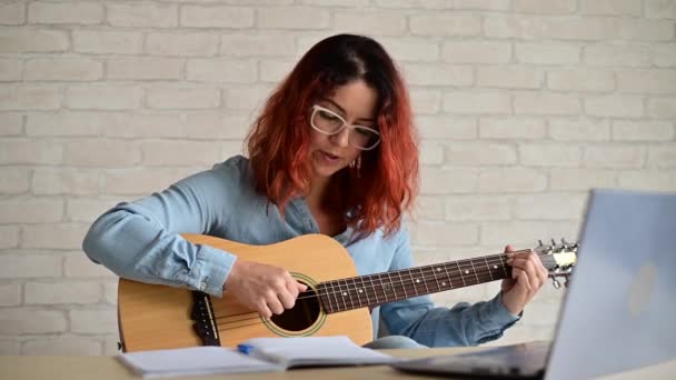 Blanke vrouw die online gitaar leert spelen. Het meisje zit in quarantaine op afstand muziek te bestuderen. — Stockvideo