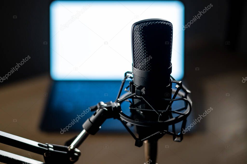 Professional microphone and laptop with white screen in the dark. Equipment in a recording and broadcasting studio