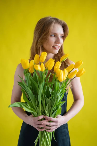 Caucasian woman with an armful of yellow tulips on a yellow background. International Womens Day. Bouquet of spring flowers — Stock Image Caucasian woman with an armful of yellow tulips on a yellow background. International Womens Day. Bouquet of spring flowers Stock Picture