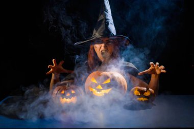 Kötü cadı balkabaklarına büyü yapıyor. Karanlıkta cadılar bayramı kostümü giymiş bir kadının portresi.