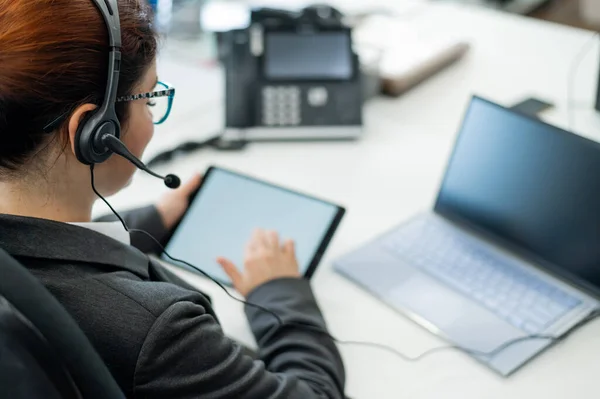 Una mujer de negocios con un auricular sostiene una tableta digital mientras está sentada en un escritorio — Foto de Stock