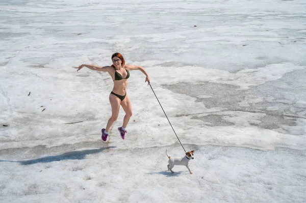 Uma mulher de biquíni caminha com um cachorro na neve — Fotografia de Stock