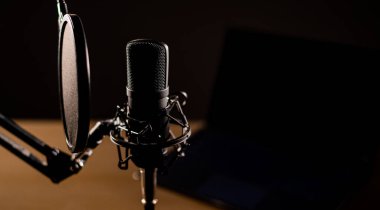 Karanlıkta dizüstü bilgisayarın arka planında profesyonel bir mikrofonun yakın plan görüntüsü