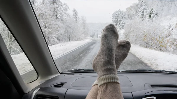 Ženské nohy ve vlněných ponožkách na palubní desce auta v zimě. Zobrazení čelního skla — Stock fotografie