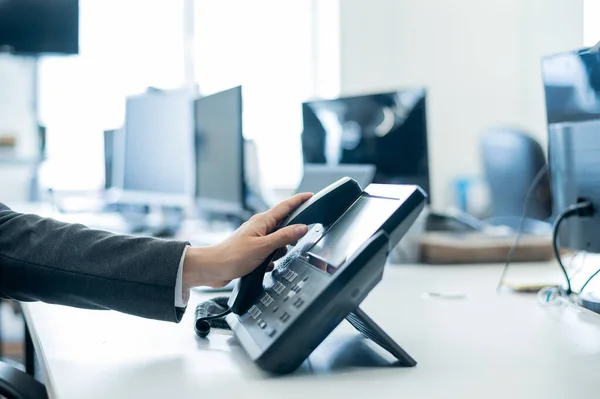 Primer plano de una empleada femenina mano en un teléfono fijo. Mujer coge un teléfono pulsador en el lugar de trabajo en la oficina — Foto de Stock