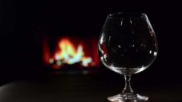 Häll brandy i ett glas mot bakgrund av den öppna spisen — Stockvideo