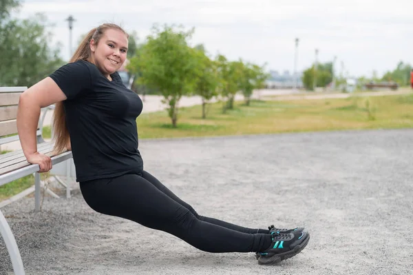 Junge dicke Frau macht Liegestütze von der Bank im Freien. Molliges Mädchen macht Fitnessübungen. — Stockfoto