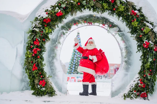 Porträtt av en äldre man klädd som tomten klo på bakgrunden av en julgran utomhus. — Stockfoto