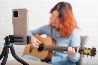 A woman is broadcasting online on her phone at home. The girl sings and plays the guitar live clipart