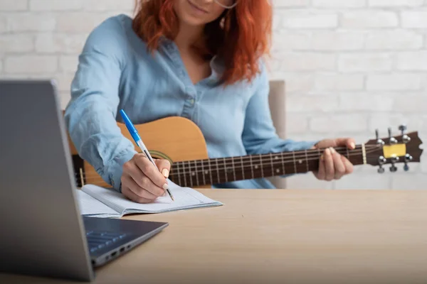 Eine Frau mit Gitarre schreibt Notizen in ein Notizbuch. Das Mädchen komponiert ein Lied — Stockfoto