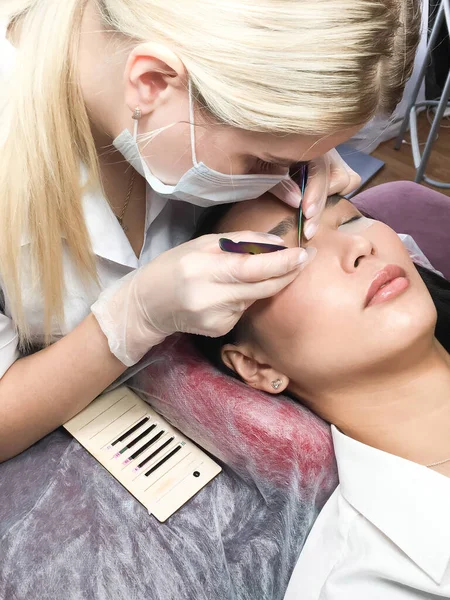 Close-up de uma bela mulher asiática no procedimento de extensão de pestanas. Cílios falsos de volume duplo. Lashmaker no trabalho. — Fotografia de Stock