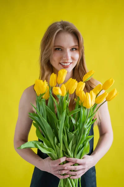 Caucasian woman with an armful of yellow tulips on a yellow background. International Womens Day. Bouquet of spring flowers — Stock Image Caucasian woman with an armful of yellow tulips on a yellow background. International Womens Day. Bouquet of spring flowers Royalty Free Stock Photos