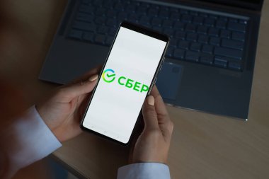 18 Ekim 2020 Rusya, Novosibirsk: Ekranda yeni Sberbank logosu olan bir kadın akıllı telefon tutuyor