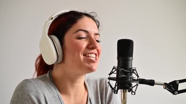Portret van een blanke vrouw in een koptelefoon zendt uit op een witte achtergrond. Toonaangevend meisje op het radiostation — Stockvideo