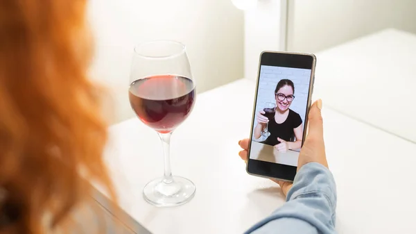 The women talk over video communication on the phone and drink red wine. The quarantined girl is not making a video call