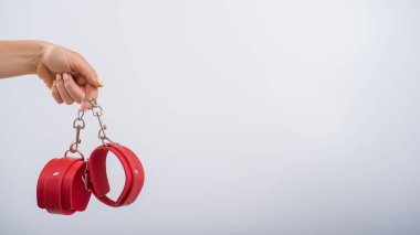 Beyaz arka planda kırmızı deri kelepçeler ve kadın elleri. BDSM aksesuarları