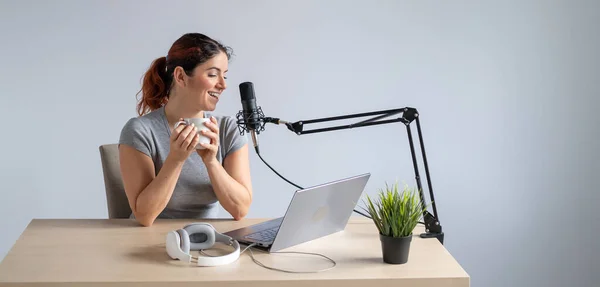 Egy nő a neten sugároz egy laptopon és kávét iszik. Női rádiós műsorvezető a munkahelyen — Stock Fotó