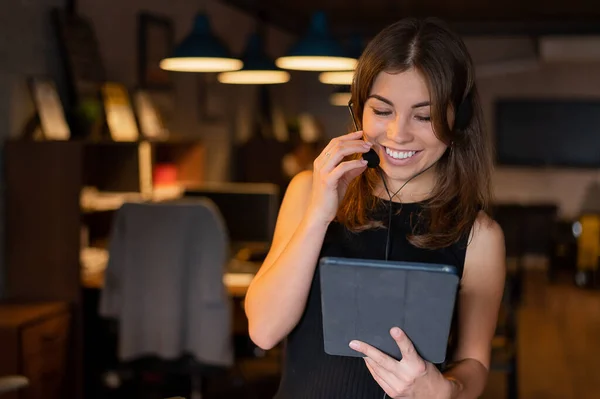 헤드폰을 쓰고 있는 아름다운 비지니스 여성이 사무실에서 디지털 태블릿을 들고 있습니다. — 스톡 사진
