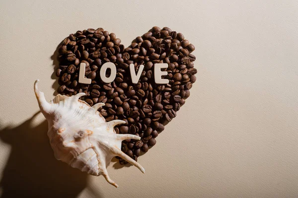 Heart shaped coffee beans lettering love and seashell. Copy space. — Stock Photo, Image