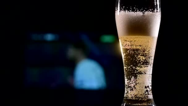 Gros plan de bière légère moussante fraîche dans un verre et de football à la télévision en arrière-plan. Concept de bar sportif — Video