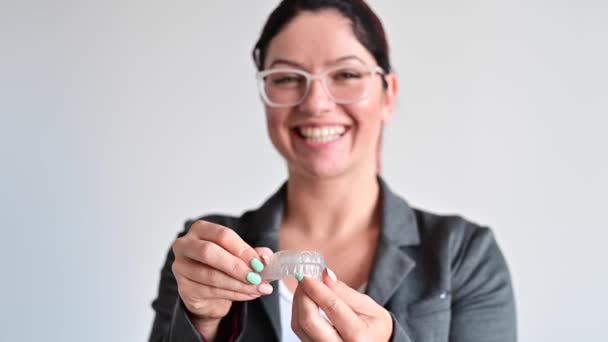 Μια γυναίκα κρατάει ένα διάφανο πλαστικό προστατευτικό στόματος. Συσκευή διόρθωσης δαγκωμάτων ορθοδοντικών — Αρχείο Βίντεο