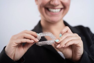 Bir kadın şeffaf plastik bir ağız koruyucusu tutuyor. Ortodontistler diş düzeltme aygıtını ısırırlar