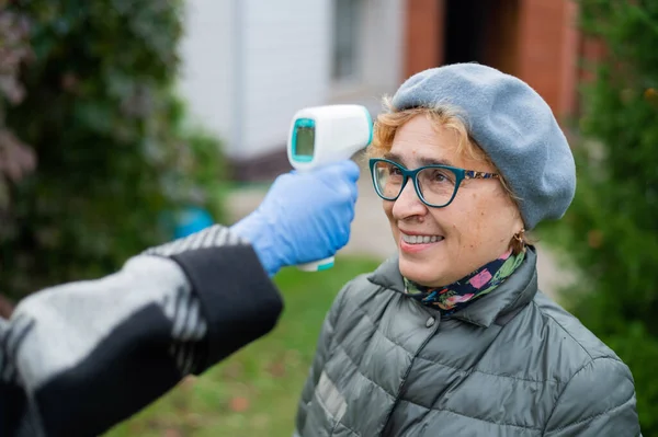Лікар вимірює температуру літньої жінки в масці з безконтактним інфрачервоним термометром на відкритому повітрі — стокове фото