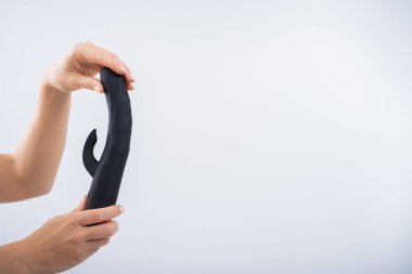 Faceless woman holding black dildo with clitoris stimulator on white background